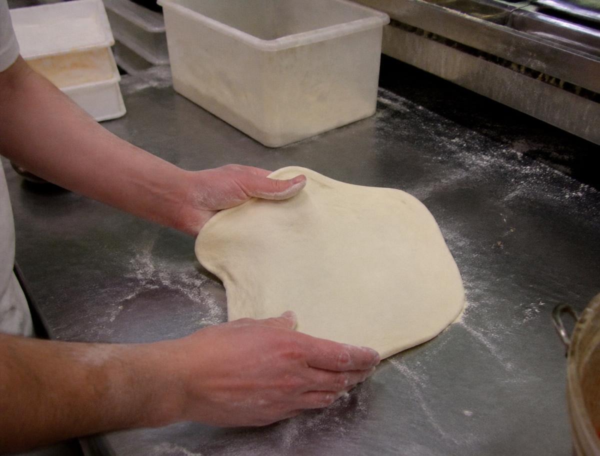 Frischer Pizzateig wird von Hand auf einer bemehlten Arbeitsfläche ausgezogen